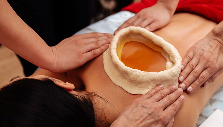 Photo of a therapist's hands shaping a dough barrier on a patient's back for deep tissue heating