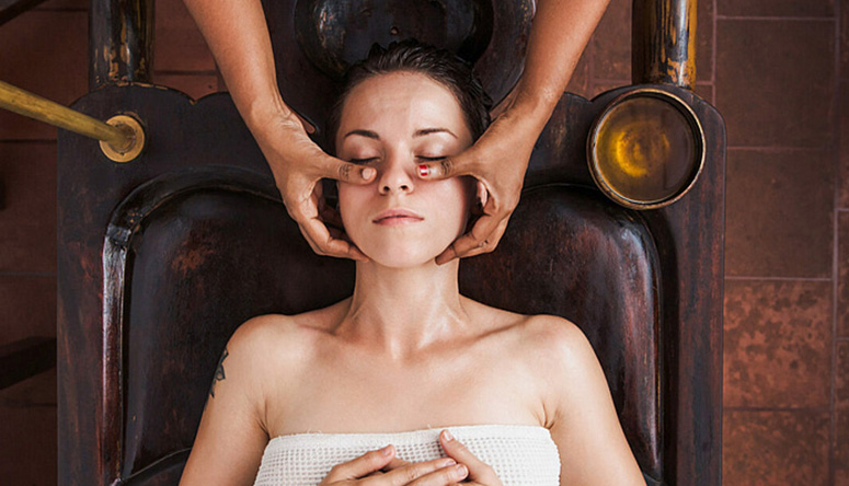 Photo of a relaxed woman getting a specialized Ayurvedic facial massage from a professional therapist.