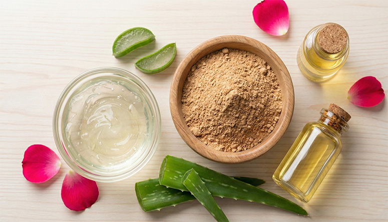 Aloe gel, sandalwood powder, oil, and rose petals arranged on a wooden table for cooling Ayurvedic summer skincare remedies.