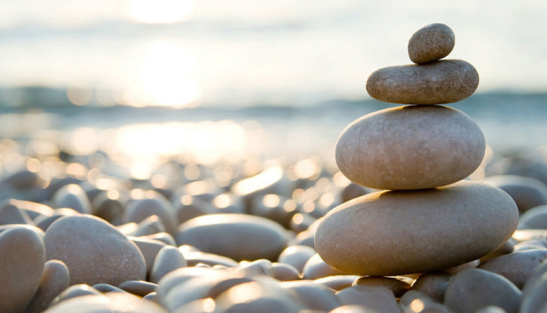 Stack of balanced zen stones on a pebble beach at sunset symbolizing the stability and grounding of the Earth element
