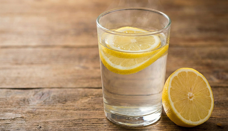 Glass of warm water with fresh lemon slices on a wooden table highlighting Ayurvedic methods for better digestion