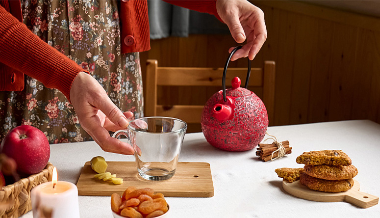 Hand reaching for glass cup near red teapot and cooling spices like ginger and fennel for Pitta balance