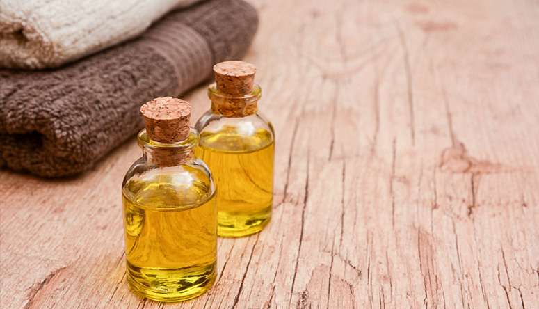 Photo of two glass bottles containing golden Ayurvedic massage oil on a textured wooden table.