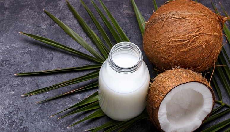 Fresh coconut water in a glass bottle with whole and halved coconuts on a palm leaf for natural hydration