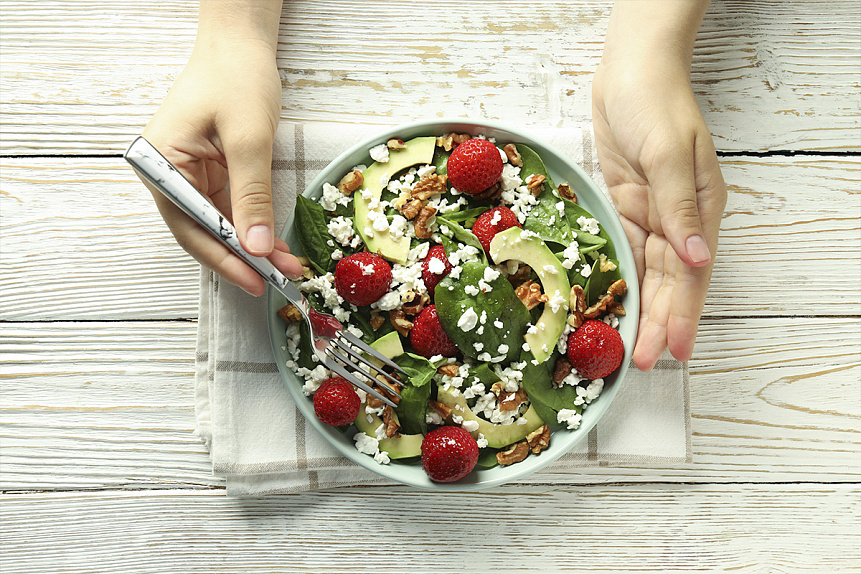 Photo of hands holding a fresh strawberry and spinach salad showing a healthy ayurvedic diet.