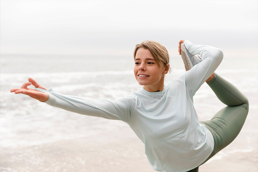Photo of a woman in a yoga pose on the beach, engaging in a physical practice to strengthen her emotional balance.