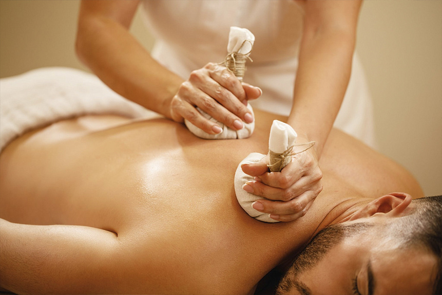 Photograph of a therapist gently pressing hot herbal bags onto a client's back during a relaxing spa treatment.