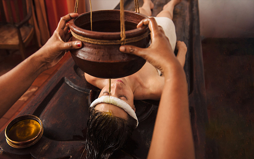 Photo of a traditional Shirodhara therapy pouring warm oil on the forehead for Ayurvedic stress relief.