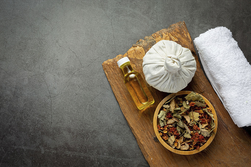 Photo of a small herbal poultice and golden oil arranged on a wooden board before starting facial spa procedures.