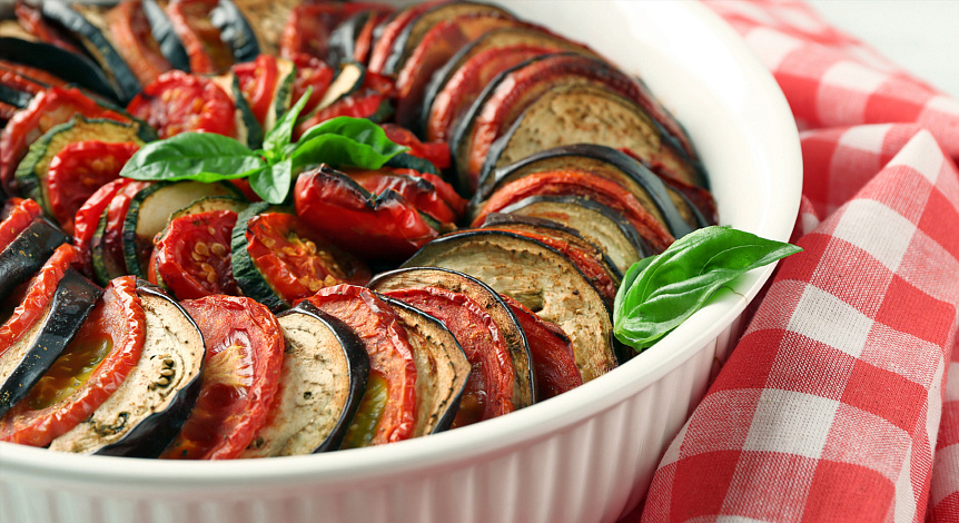 Photo of baked vegetable ratatouille garnished with fresh basil for a hearty Ayurvedic dinner.