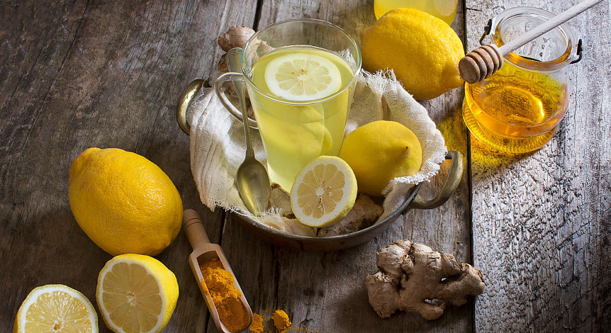 Photo of a glass mug of ginger tea with lemon and honey on a wooden board to stimulate digestion.