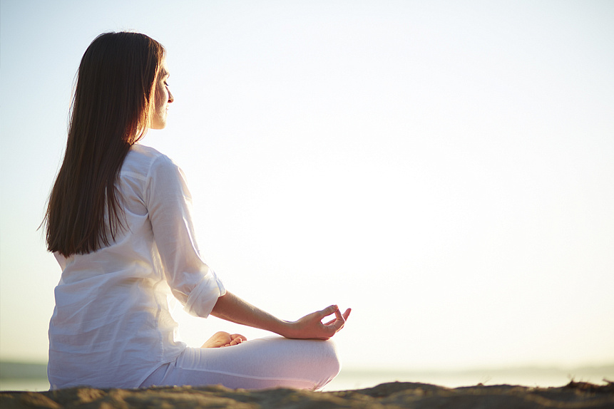 Photo of a woman meditating on a sunny beach to harmonize energy and transform internal blocks.