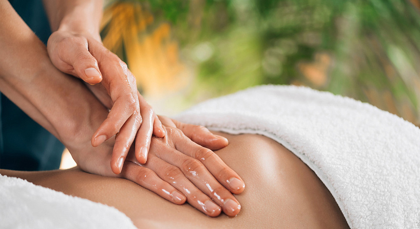 Photo of a therapist's hands rubbing warm sesame oil into a back to balance vata dosha in winter.