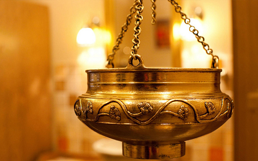 Photo of an ornate brass Dhara Patra vessel hanging on metal chains for Shirodhara clinic equipment.