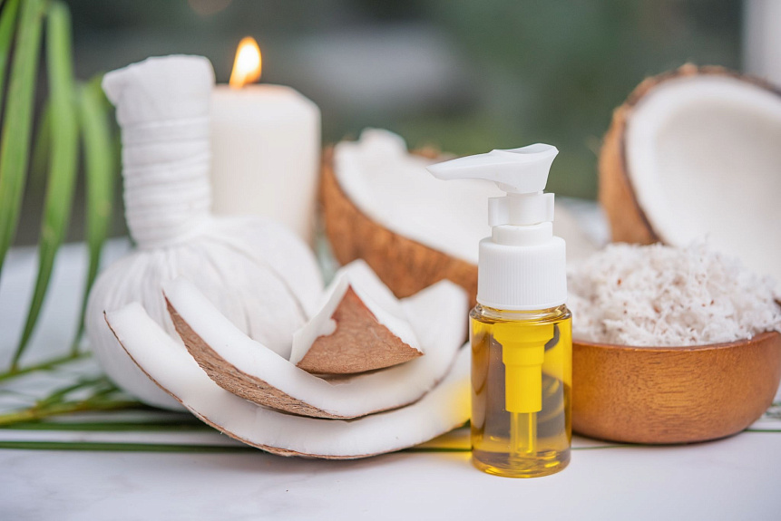 Photo of a clear dispenser bottle with golden oil among fresh coconuts and spa accessories for personalized care