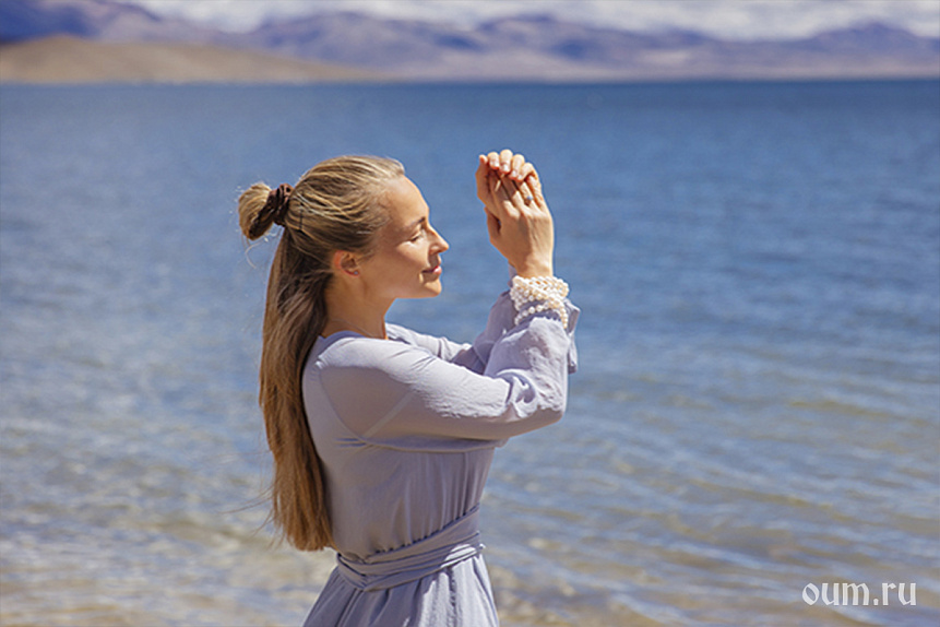Photo of a woman standing with closed eyes by a mountain lake embracing ayurvedic morning rhythms.