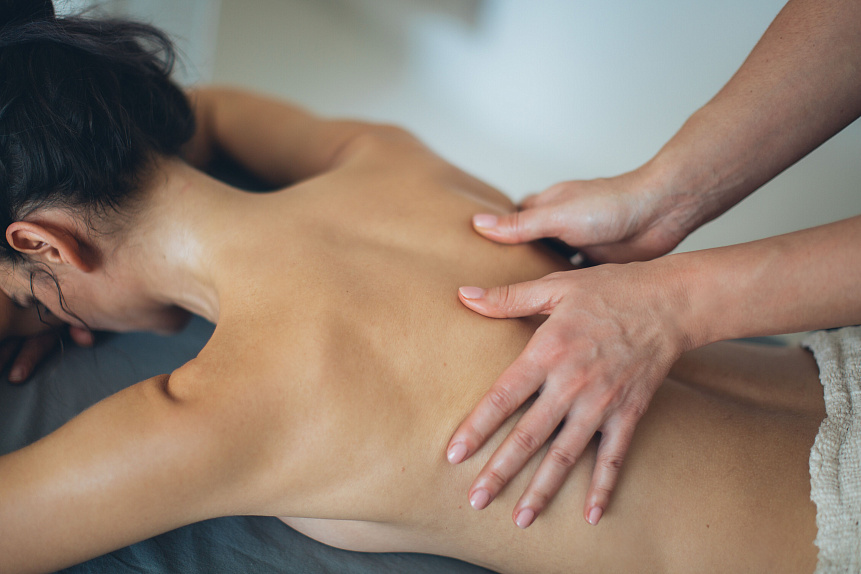 Photo of a therapist's hands rubbing warm sesame oil into a back to balance vata dosha in winter.