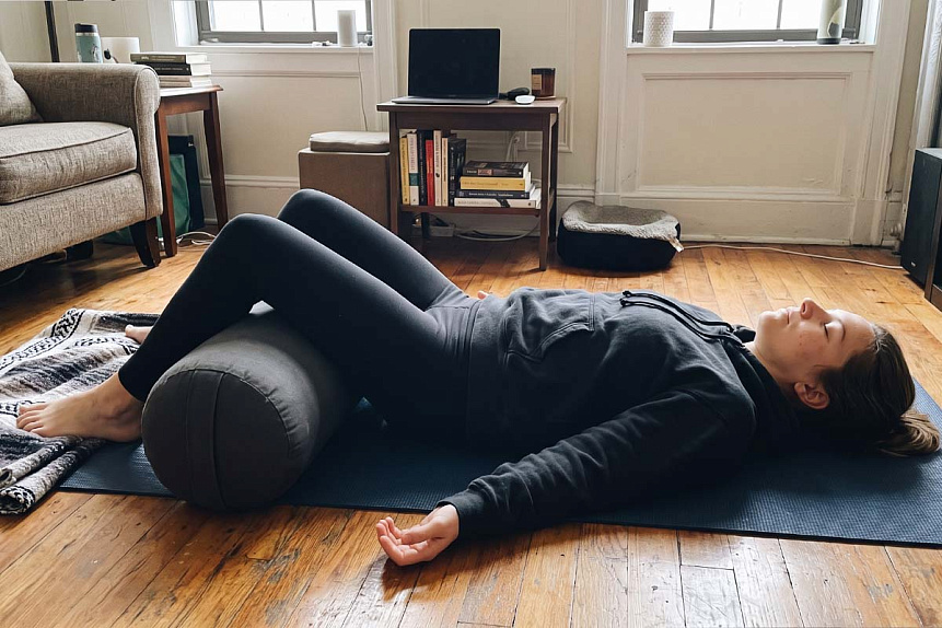 Lifelike photograph of a woman resting on a mat in savasana with a bolster placed under her knees