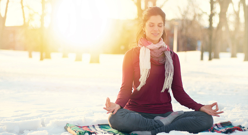 Photo of a woman meditating in lotus pose on the snow to preserve energy during winter.