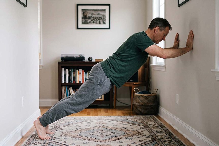 Realistic photo of a man doing a therapeutic wall plank exercise in a natural home environment