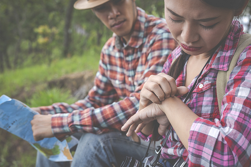 Photo of a woman scratching a mosquito bite in the forest illustrating the discomfort caused by insects in nature.
