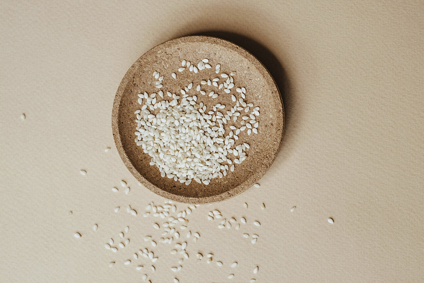 Photo of white sesame seeds in a round cork plate serving as a base ingredient for Ayurvedic formulations
