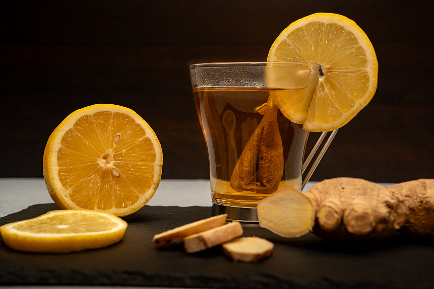 Photo of a glass mug of ginger tea with lemon and honey on a wooden board to stimulate digestion.