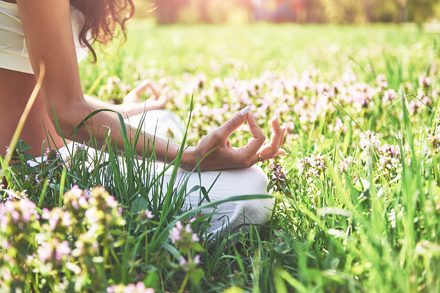 Photo of a woman's hands in a mudra during meditation in a blooming meadow for spiritual harmony.