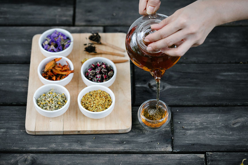 Hand reaching for glass cup near red teapot and cooling spices like ginger and fennel for Pitta balance