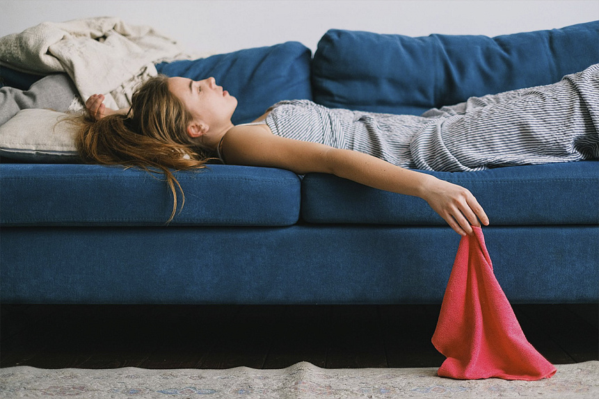 Photograph of an exhausted woman lying on a sofa experiencing iron deficiency fatigue