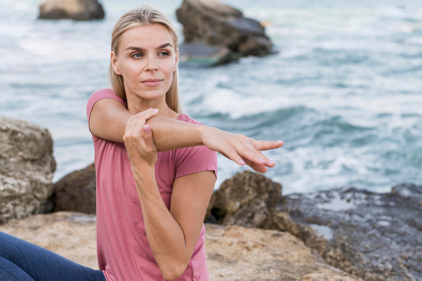 Photo of a young woman stretching arms by the ocean practicing daily physical activity for health.