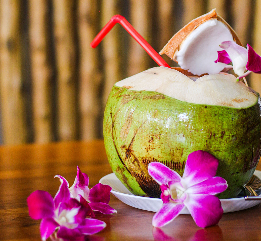Fresh coconut water in a glass bottle with whole and halved coconuts on a palm leaf for natural hydration