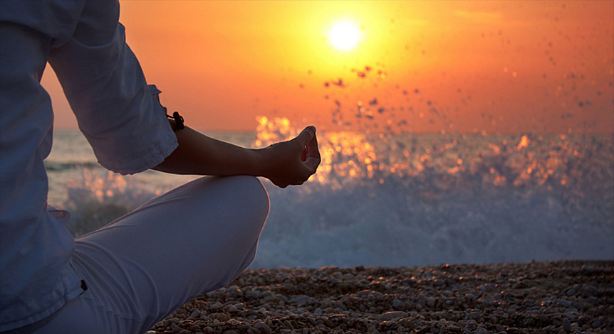 Person meditating on a beach at sunset to start the restorative Empty Bowl practice.