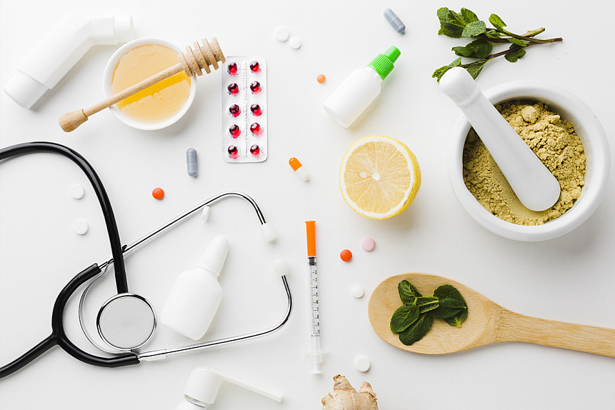 Photo of a stethoscope and fresh herbs lying together on a white surface representing modern medicine and Ayurveda.