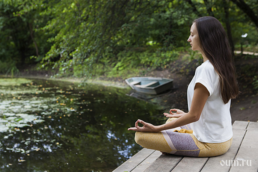 Photo of a woman meditating by a calm forest lake finding ayurvedic mental balance.