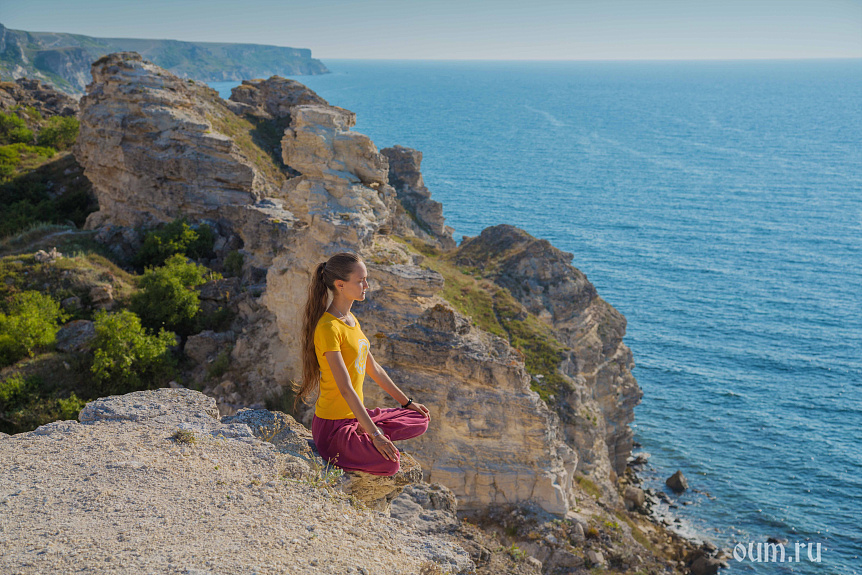 Photo of a woman meditating on a rocky cliff by the ocean demonstrating two-way attention practice.